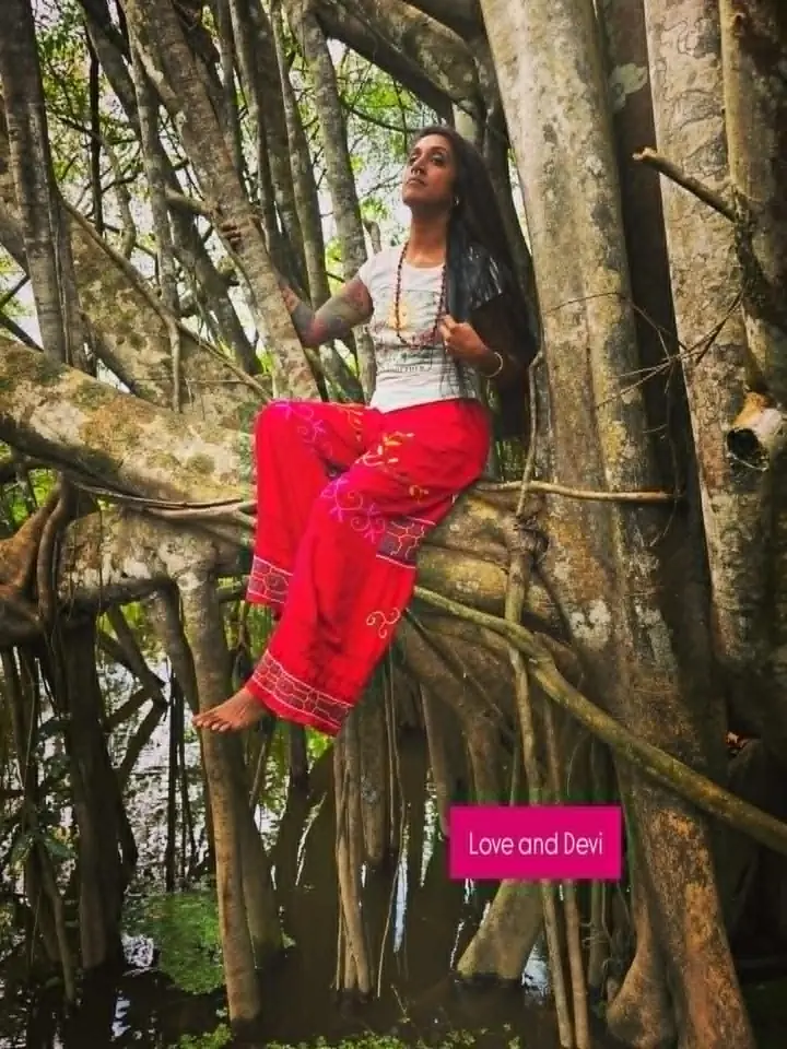 Natasha Devi seated among the roots of a large rainforest tree.